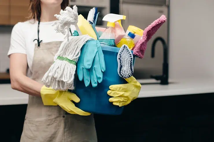 A woman holding a bucket of cleaning supplies.