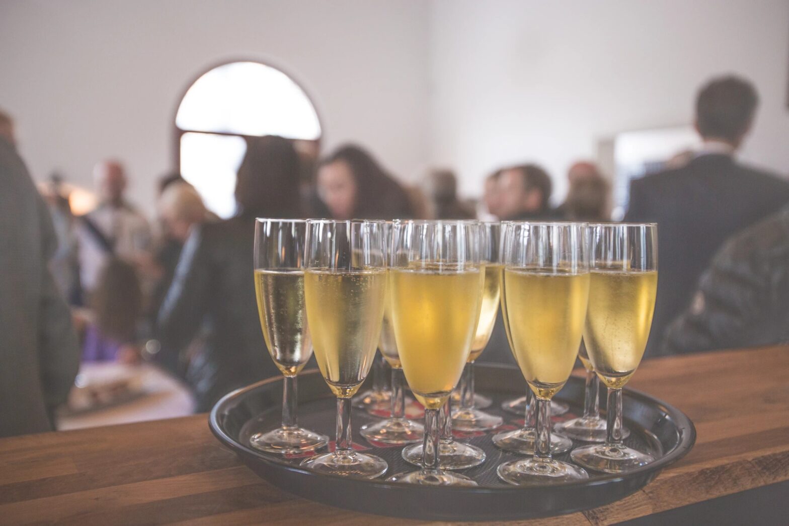 A tray of champagne glasses on a table in front of a group of people.